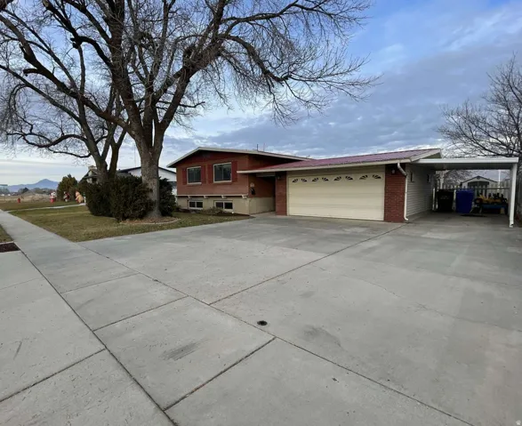 Split level home with driveway, an attached carport, brick siding, and a garage