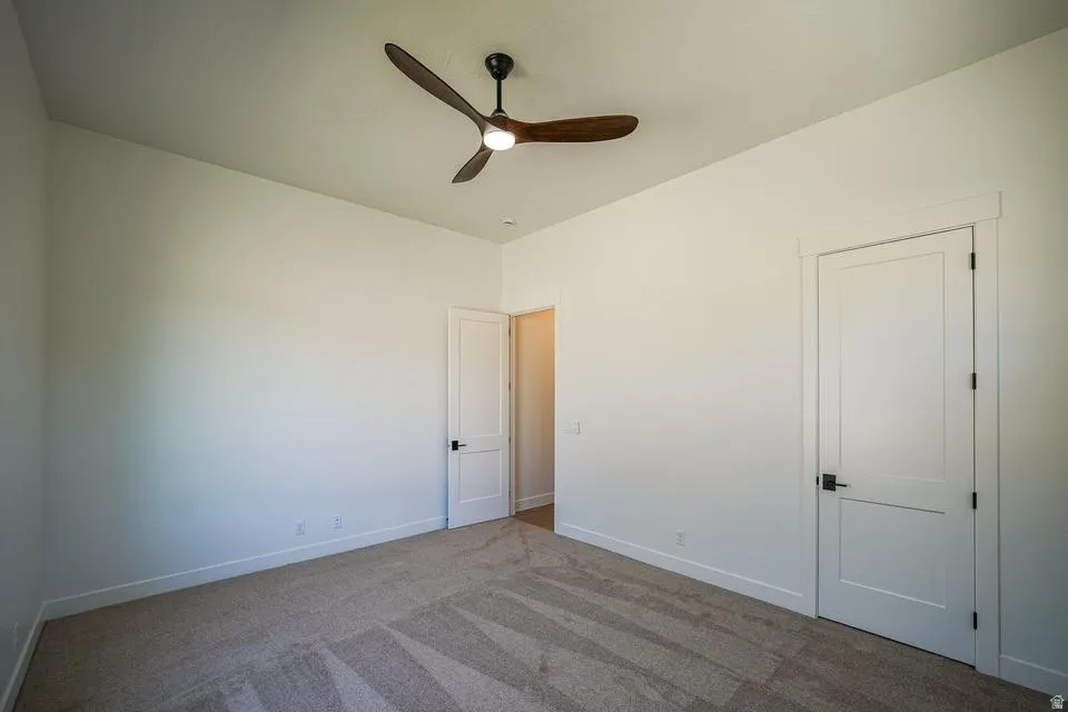 Spacious room featuring neutral carpeting, a modern ceiling fan with integrated lighting, and two panel doors with matte black hardware