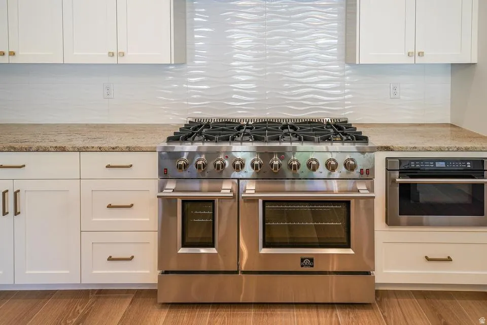 Stainless steel professional-grade range with double ovens, integrated microwave, white shaker cabinetry, granite countertops, and a textured white tile backsplash
