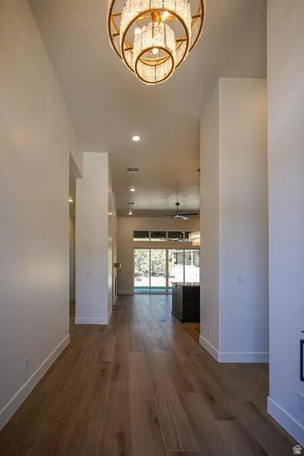 Hallway featuring a tiered chandelier, recessed lighting, wood-finish flooring, and white baseboards, opening to a bright area with full-height glass doors