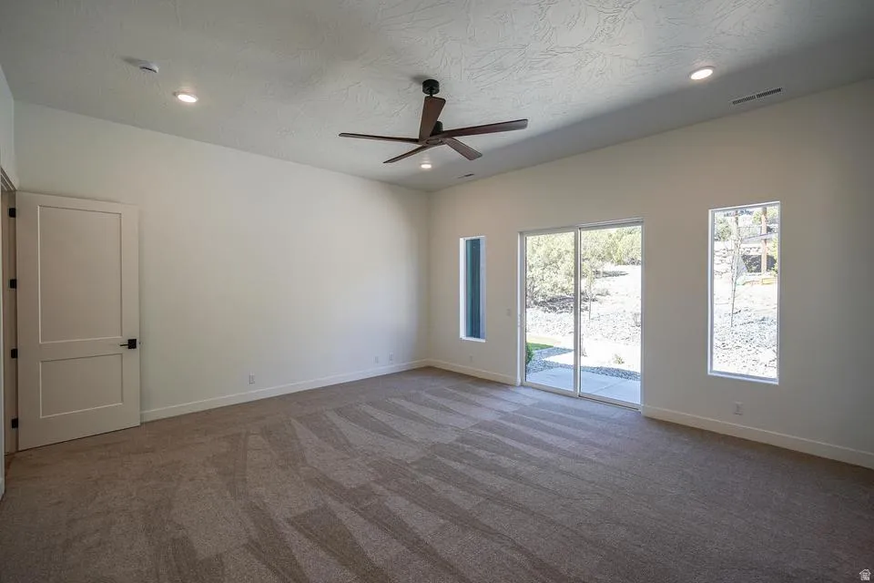 Spacious room featuring neutral carpet flooring, recessed lighting, and a dark wood-finish ceiling fan