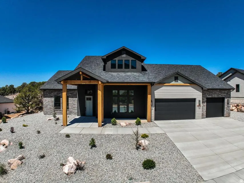 Contemporary exterior featuring a covered entry with wood-tone columns, dark gray siding, natural stone accents, a multi-pane front door, and a two-car garage with dark paneled doors