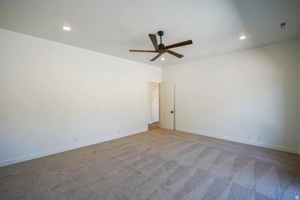 Spacious room featuring neutral carpeting, a ceiling fan with dark wood-finish blades, recessed lighting, and white walls