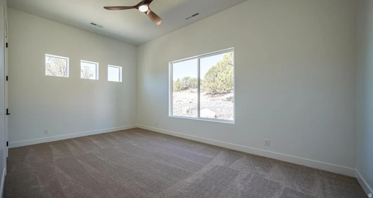 Spacious room featuring neutral carpet flooring, a large picture window, three transom windows, a modern ceiling fan, and white baseboards