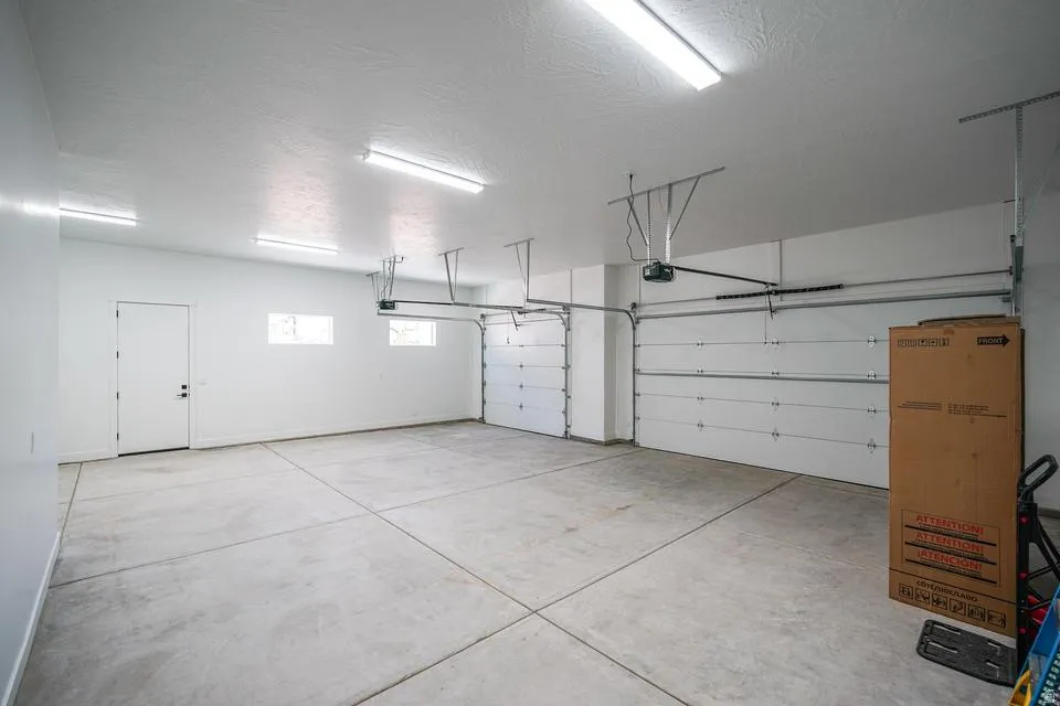 Spacious multi-car garage featuring a concrete floor, two overhead doors, and ceiling-mounted fluorescent lighting