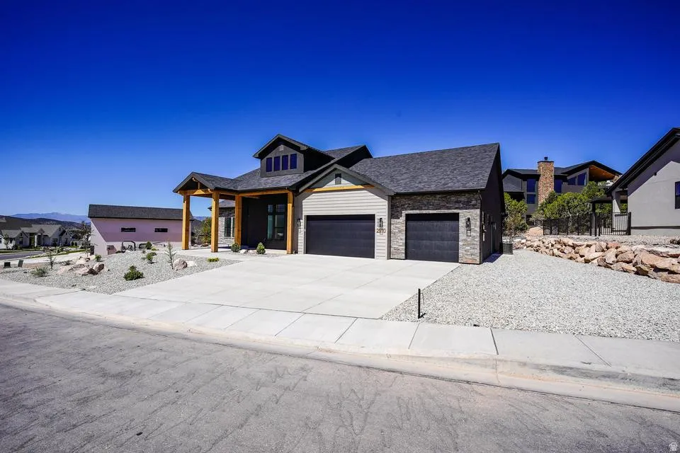 Contemporary exterior featuring a stone and siding facade, a two-car garage with dark paneled doors, and a covered entry with exposed wood beams