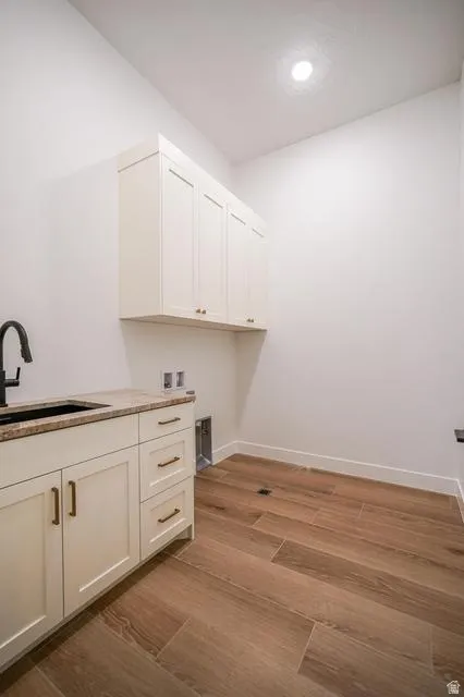 Utility area featuring wood-finish tile flooring, white cabinetry with bronze hardware, and a dark stone countertop with an undermount sink