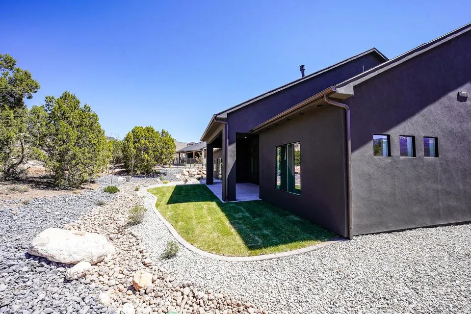 Contemporary dark stucco exterior with a covered patio, framed by mature trees