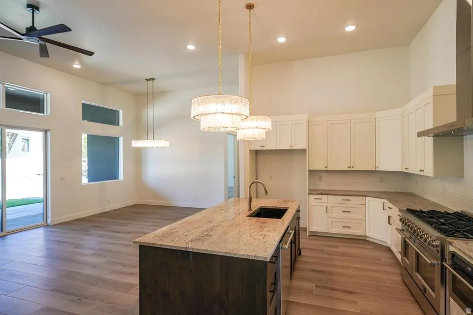 Gourmet kitchen and living area featuring high ceilings, wood-finish flooring, a central island with an undermount sink, stainless steel appliances, and white cabinetry