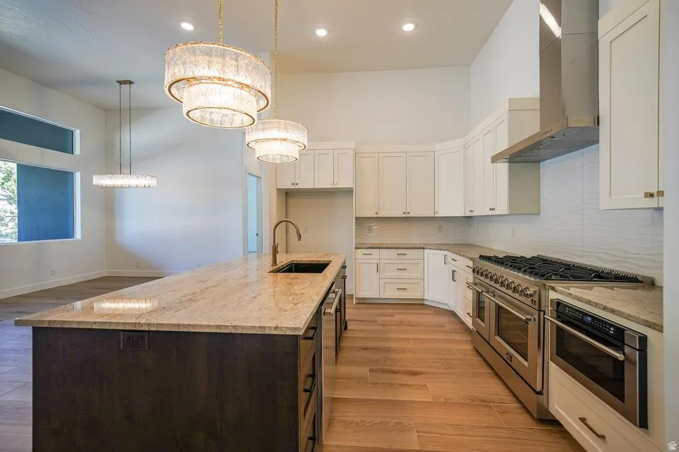 Gourmet kitchen featuring a large central island with an undermount sink and faucet, integrated stainless steel appliances, white shaker cabinetry, and wood-finish flooring