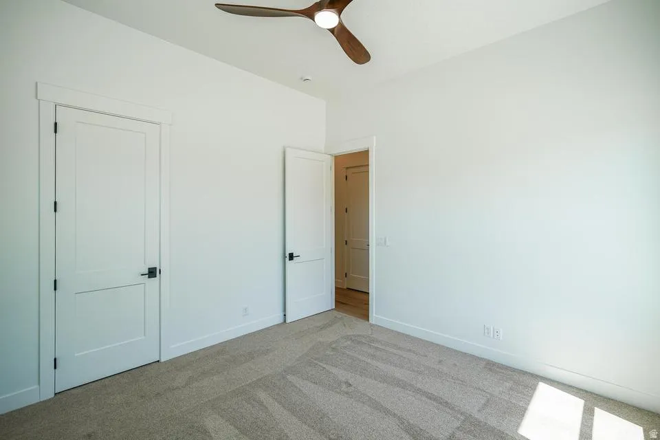 Carpeted room featuring a modern ceiling fan with wood-finish blades, white paneled doors, and contemporary black hardware