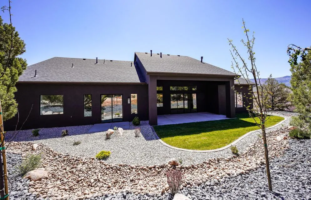 Contemporary exterior featuring an expansive concrete patio, a manicured lawn area, and a xeriscaped landscape with diverse gravels and natural rock elements
