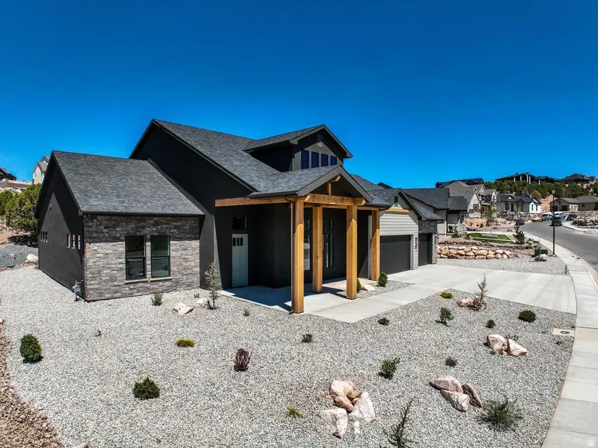 Modern exterior featuring dark gray siding with stone veneer accents, a prominent covered entry with natural wood posts, a two-car garage, and a gravel front yard with sparse landscaping