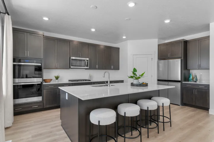 Kitchen featuring appliances with stainless steel finishes, recessed lighting, an island with sink, dark brown cabinetry, and light wood-style flooring