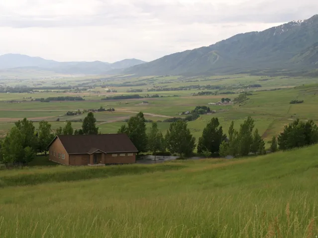 Brick exterior structure with a dark shingle roof, set against a backdrop of rolling green hills and distant mountains