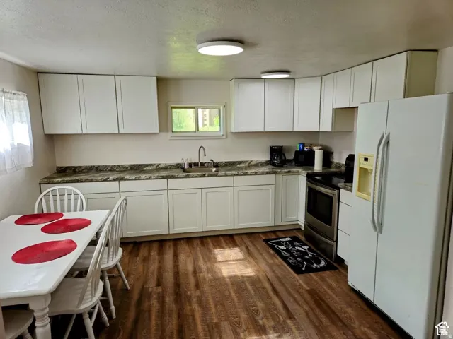 Kitchen with white refrigerator with ice dispenser, white cabinets, electric stove, a textured ceiling, and dark wood-type flooring