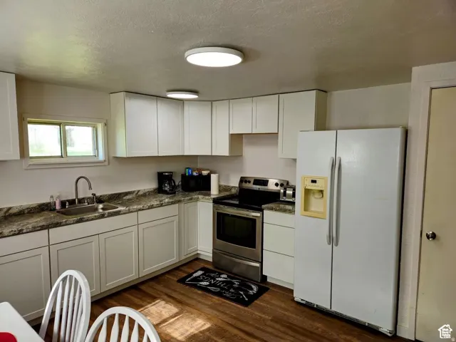 Kitchen with white refrigerator with ice dispenser, stainless steel electric range oven, a textured ceiling, white cabinetry, and dark wood-type flooring