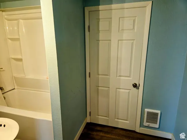 Full bathroom with dark wood-style flooring, heating unit, and tub / shower combination