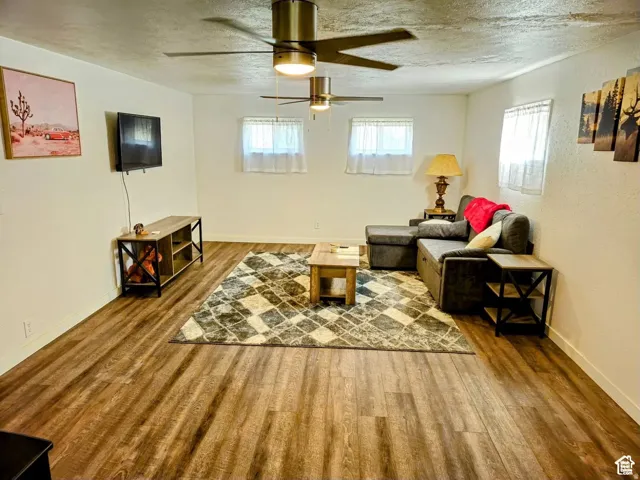 Living area with a textured ceiling, wood finished floors, a textured wall, and a ceiling fan