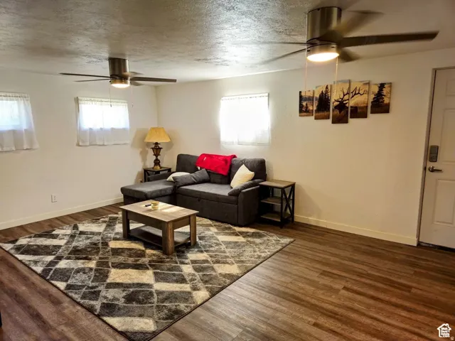 Living room with ceiling fan, a textured ceiling, and dark wood-style floors