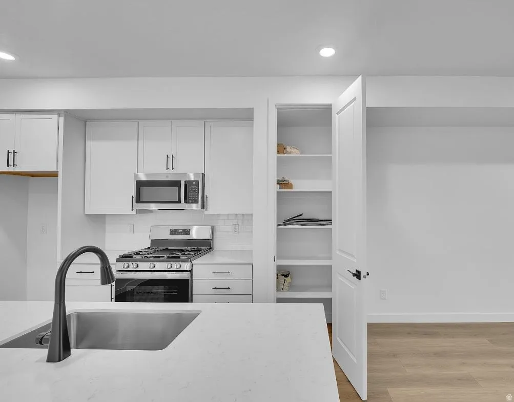 Kitchen featuring appliances with stainless steel finishes, white cabinets, light wood finished floors, decorative backsplash, and recessed lighting