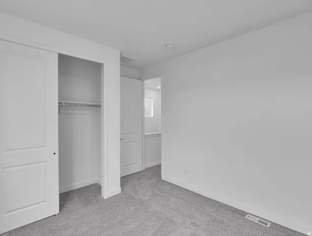 Unfurnished bedroom with light carpet and a closet