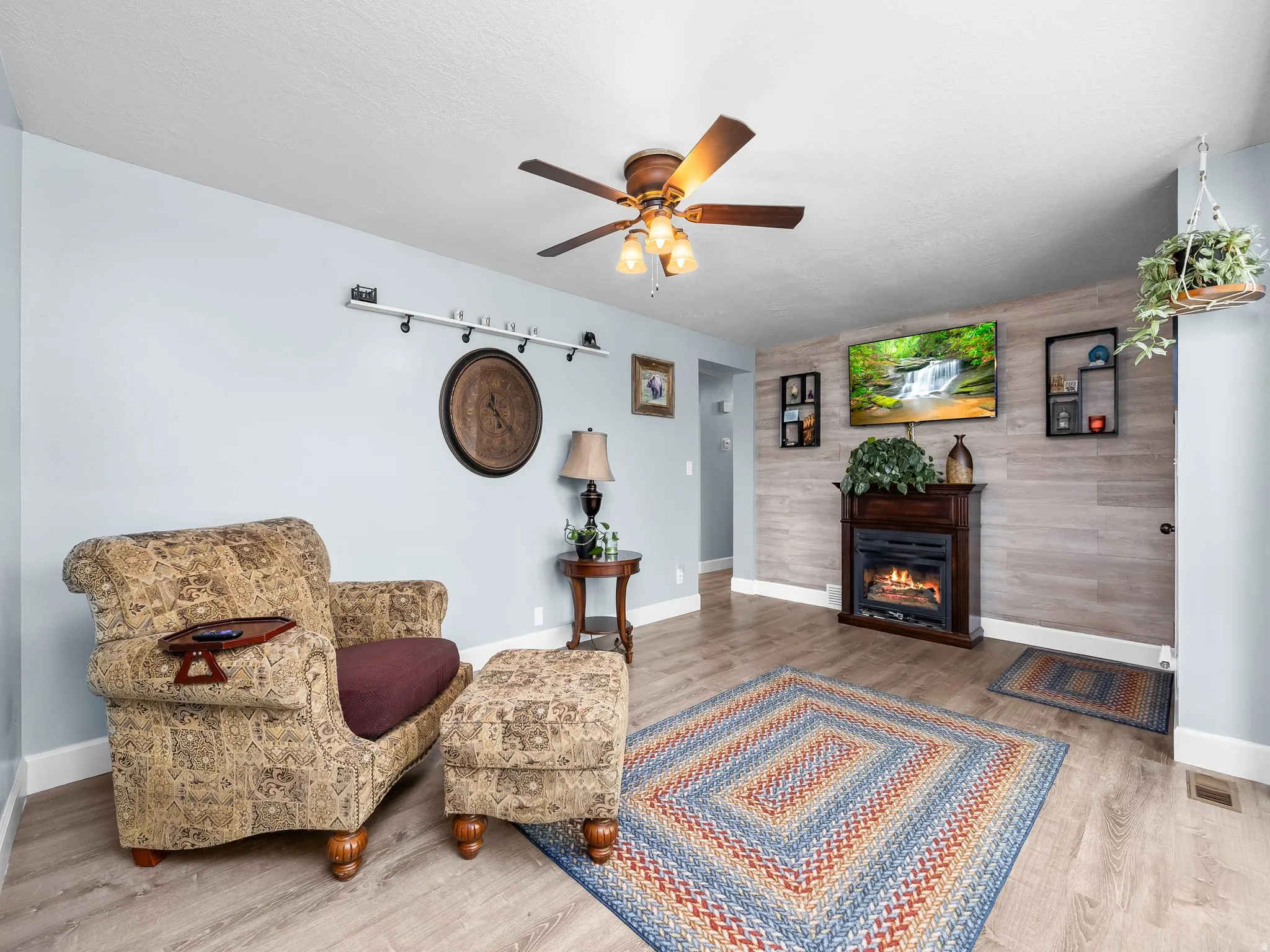 Living area featuring an accent wall, wood finished floors, a ceiling fan, a glass covered fireplace, and wooden walls
