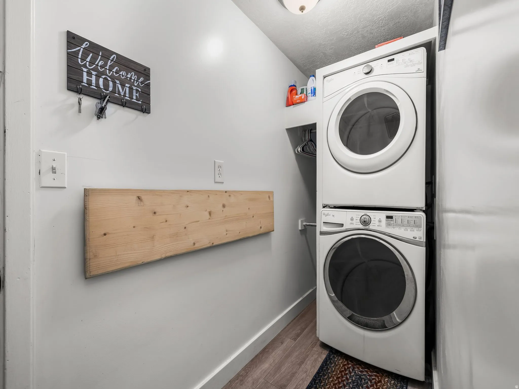 Laundry area with stacked washer / drying machine and wood finished floors
