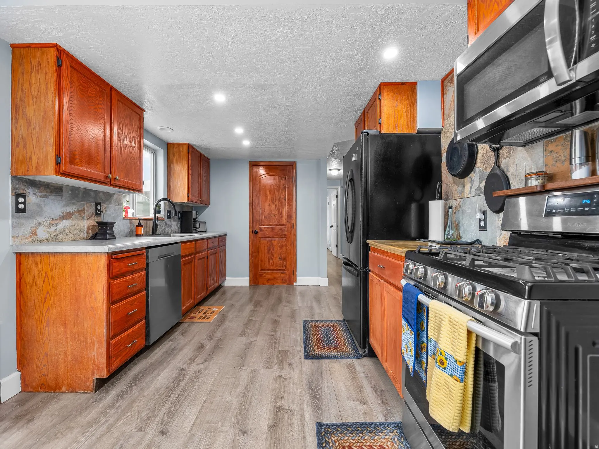Kitchen with tasteful backsplash, stainless steel appliances, light countertops, recessed lighting, and brown cabinets
