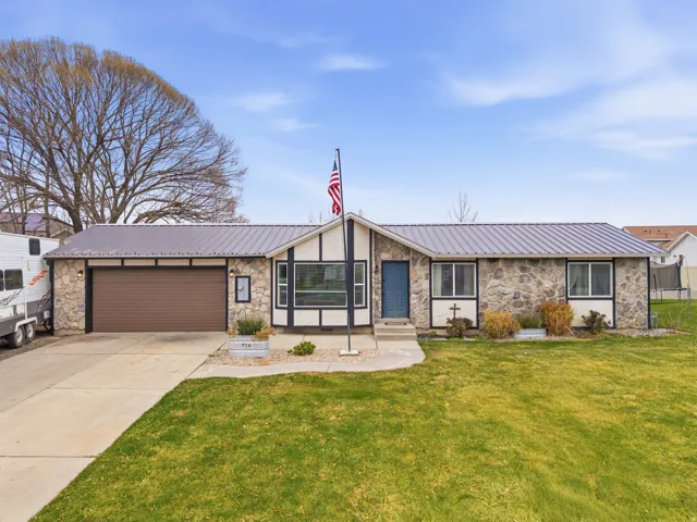View of front of home with stone siding, a metal roof, a front yard, and concrete driveway