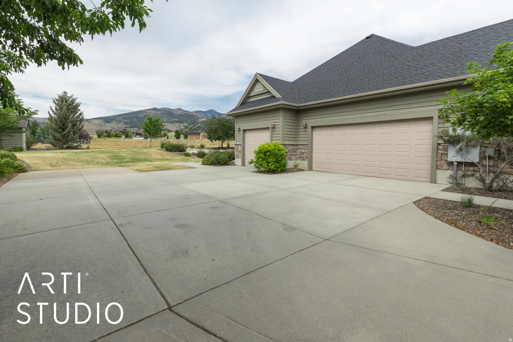 View of side of property with a yard, concrete driveway, roof with shingles, stone siding, and a mountain view