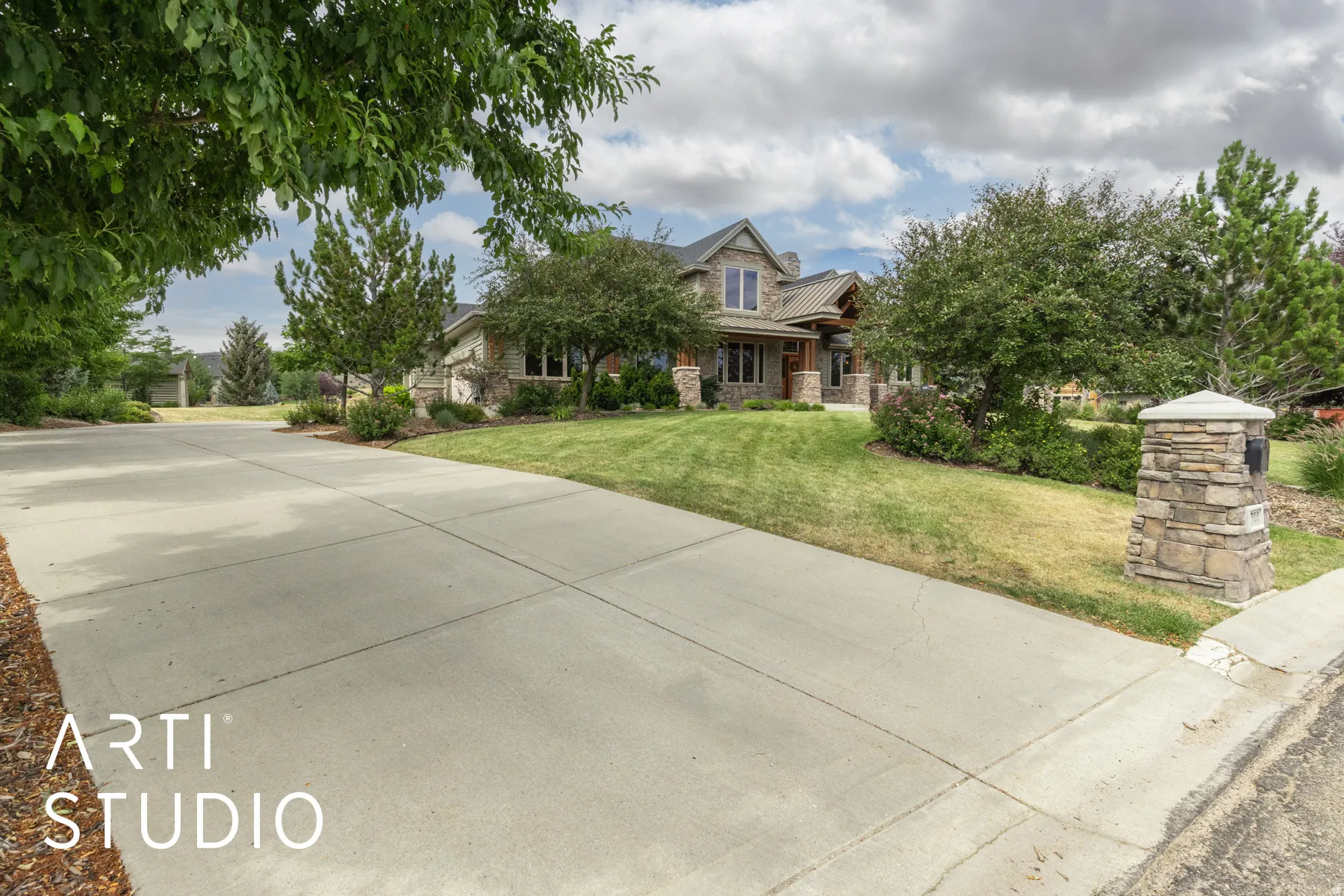 View of front facade featuring stone siding, a front lawn, concrete driveway, and covered porch