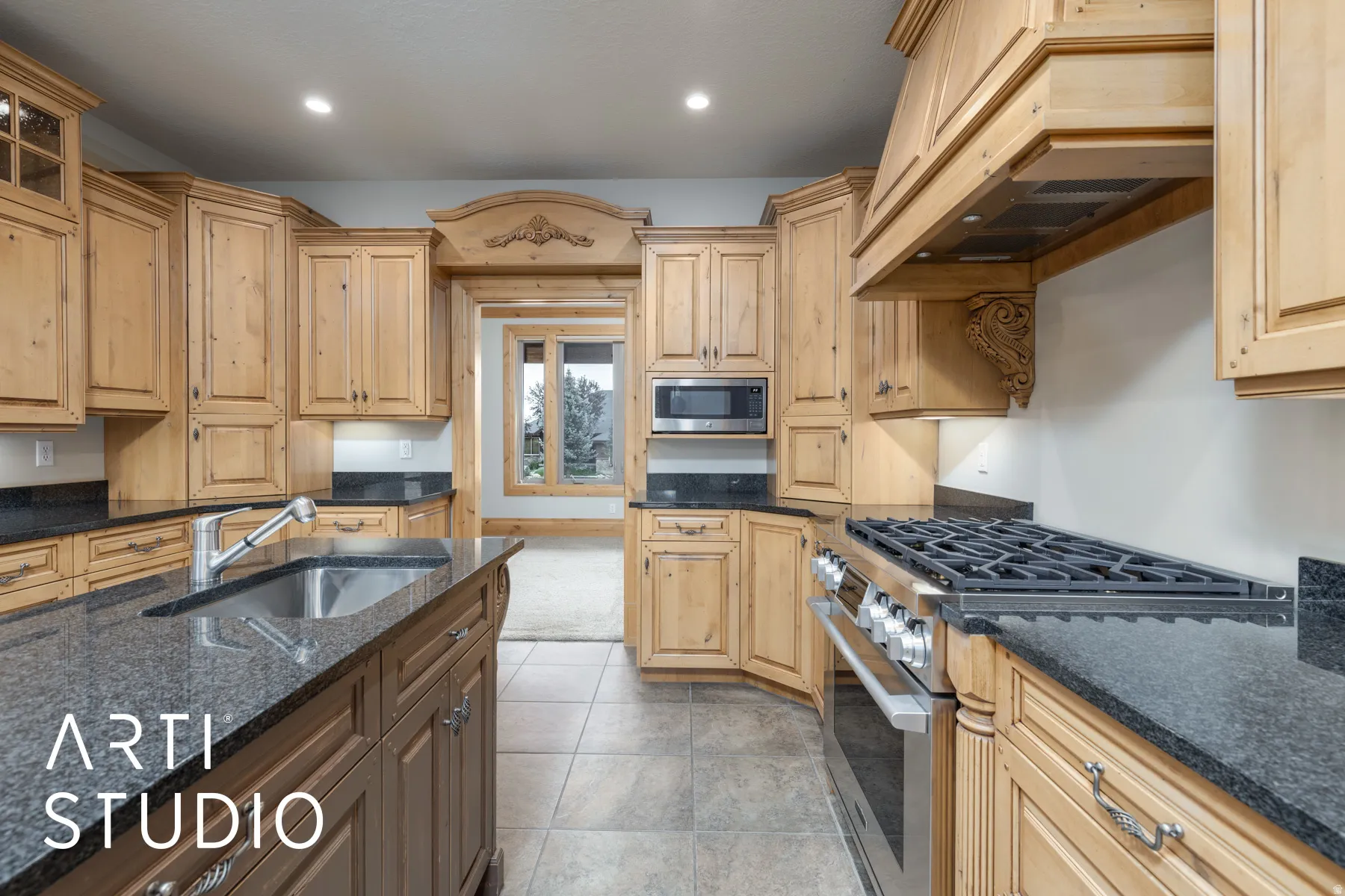 Kitchen featuring stainless steel appliances, custom range hood, dark stone counters, light brown cabinetry, and recessed lighting