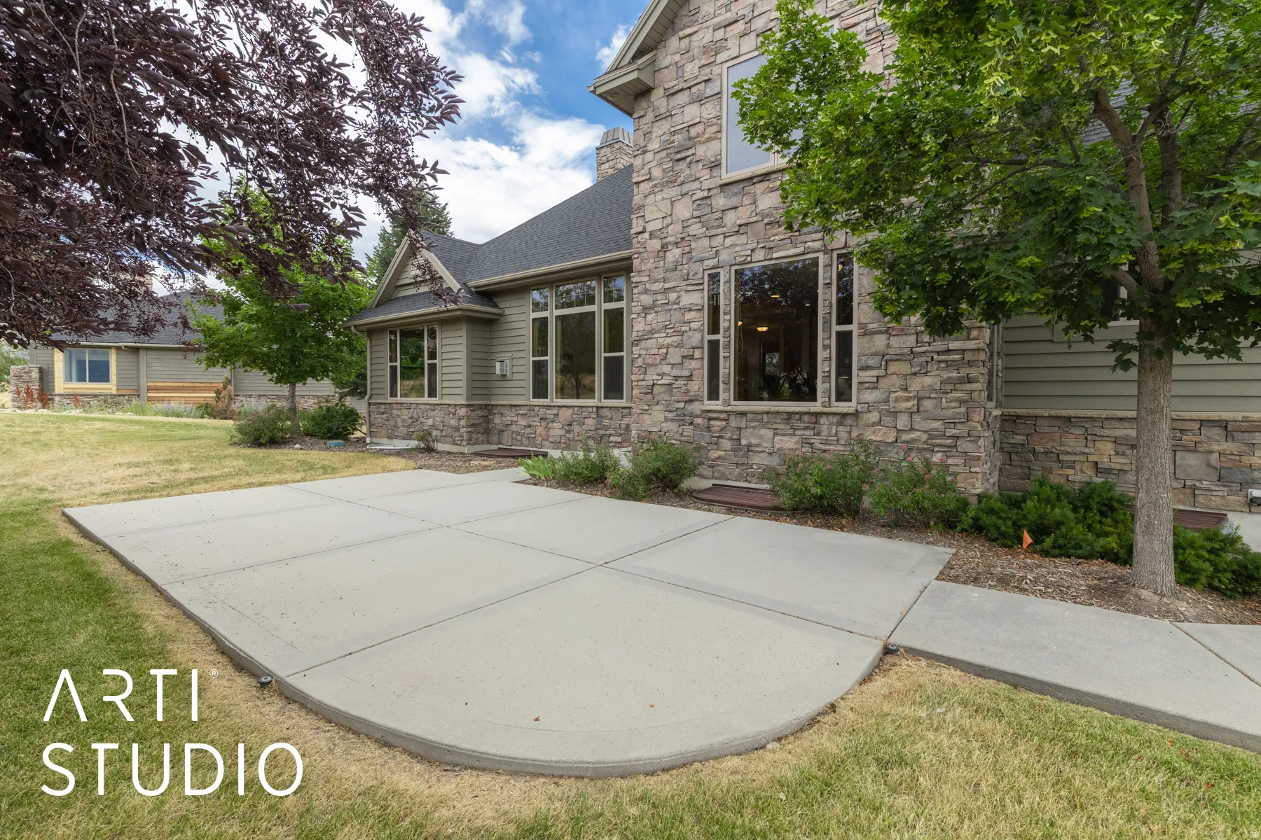 Rear view of house with a lawn, stone siding, and a patio area
