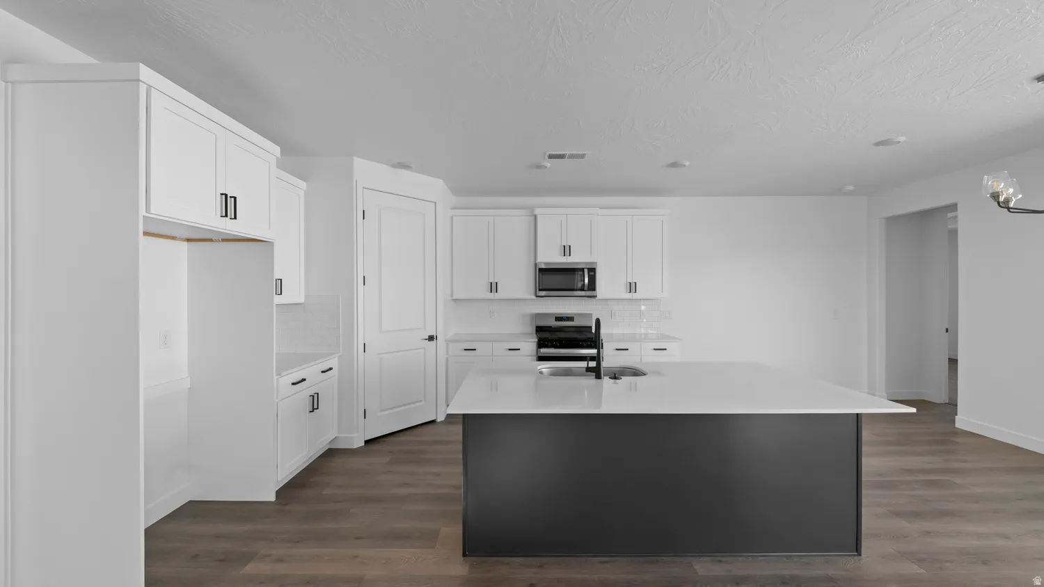 Kitchen with light stone counters, dark wood-style floors, a kitchen island with sink, stainless steel appliances, and two tone cabinets