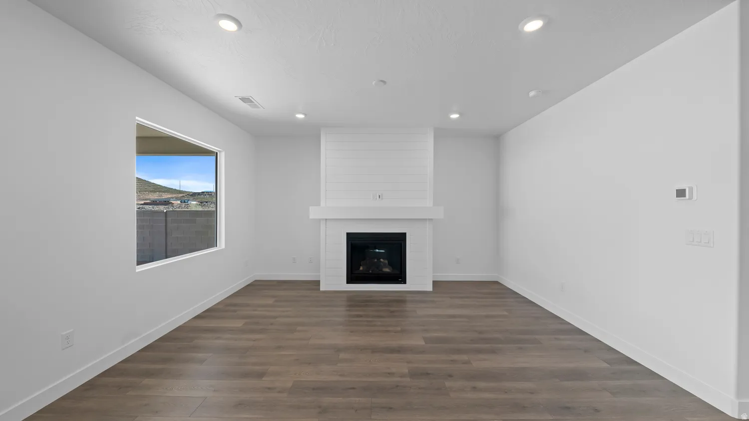 Unfurnished living room with dark wood-type flooring, a large fireplace, and recessed lighting