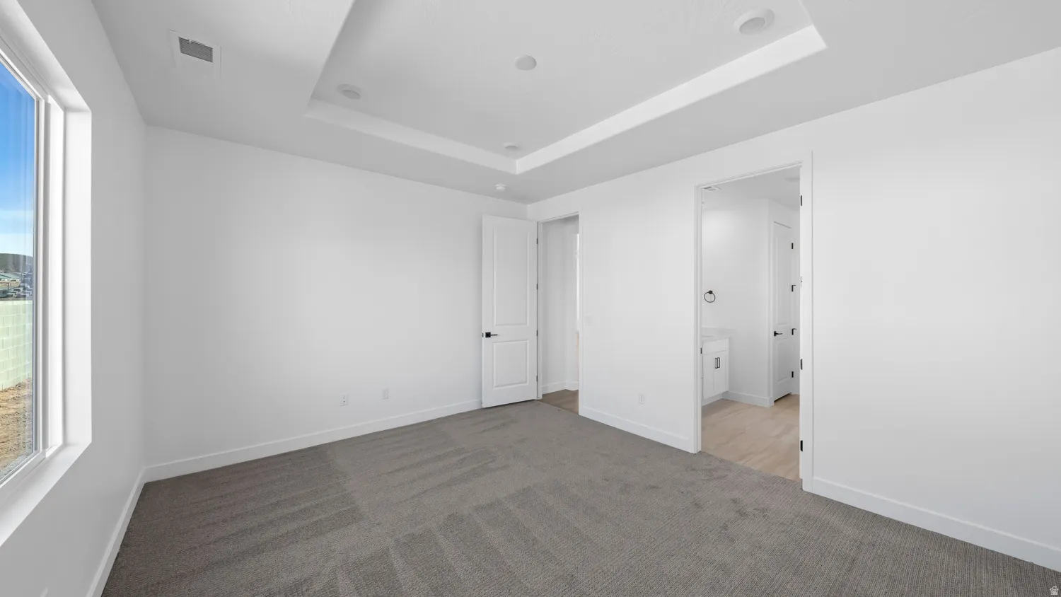 Unfurnished bedroom featuring light colored carpet, a raised ceiling, and ensuite bathroom