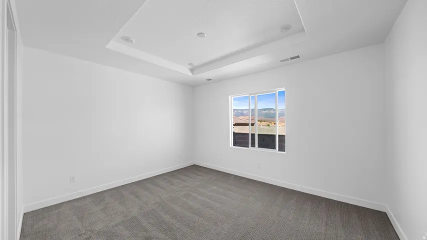 Empty room featuring dark colored carpet and a tray ceiling