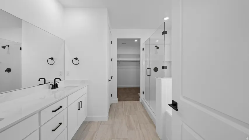 Full bath with a shower stall, double vanity, a spacious closet, and recessed lighting