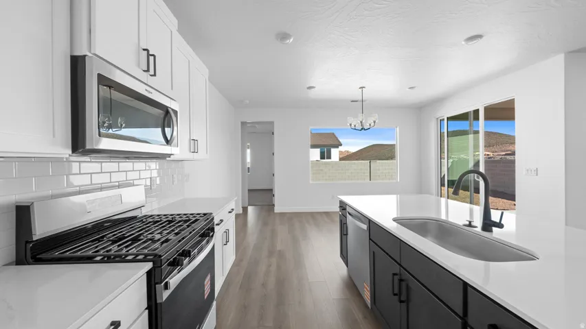 Two tone kitchen featuring stainless steel appliances, two tone color scheme, light wood-type flooring, light stone countertops, and a chandelier