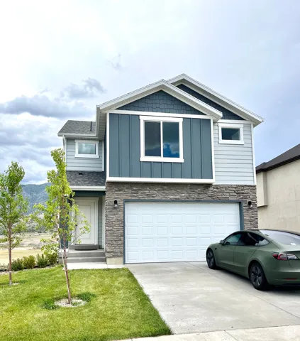 View of front of house featuring stone siding, concrete driveway, board and batten siding, an attached garage, and a front lawn