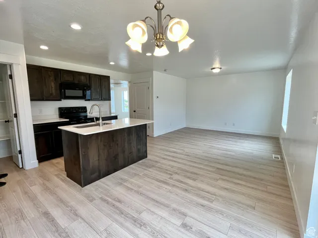 Kitchen featuring dark brown cabinetry, decorative light fixtures, an island with sink, black appliances, and a chandelier