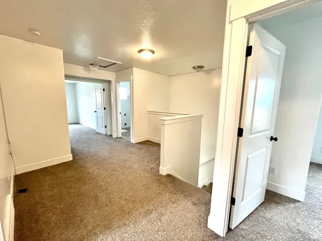 Corridor with an upstairs landing, a textured ceiling, light carpet, and attic access