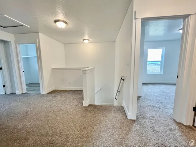 Corridor featuring an upstairs landing, a textured ceiling, and light carpet