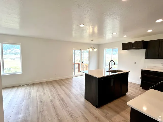 Kitchen with a kitchen island with sink, light wood finished floors, a textured ceiling, hanging light fixtures, and a chandelier