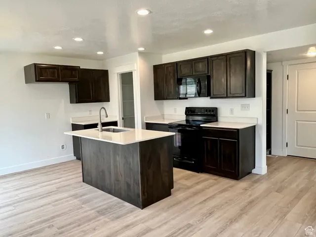 Kitchen with black appliances, dark brown cabinetry, recessed lighting, a kitchen island with sink, and light wood-style flooring
