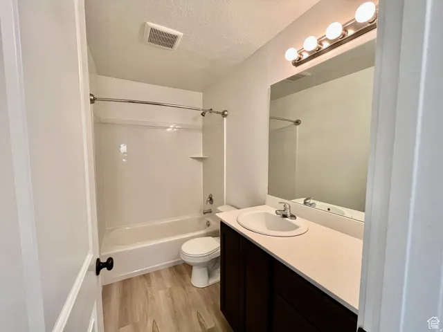 Bathroom featuring vanity, washtub / shower combination, a textured ceiling, and light wood-style floors