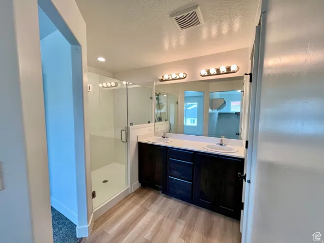 Bathroom with a textured ceiling, double vanity, a shower stall, and light wood-style floors