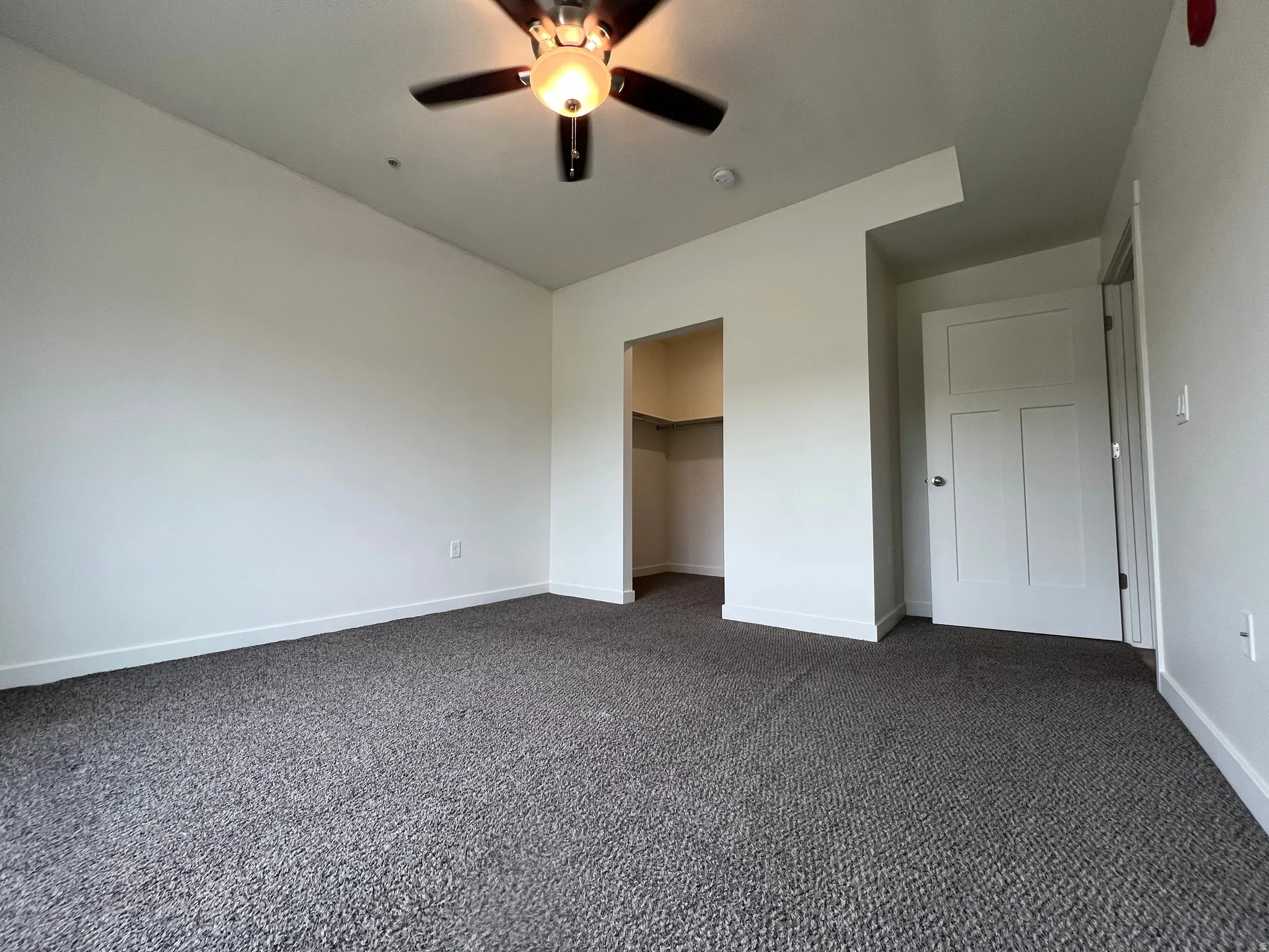 Unfurnished bedroom with dark carpet, a spacious closet, and a ceiling fan