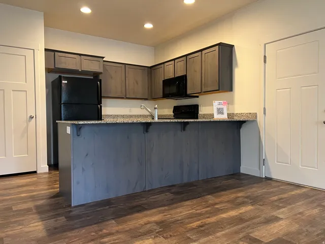 Kitchen with light stone counters, recessed lighting, a breakfast bar area, dark wood-style floors, and black appliances